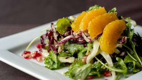 A fresh salad served with thin slices of orange on top.