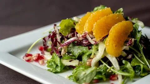 A fresh salad served with thin slices of orange on top.