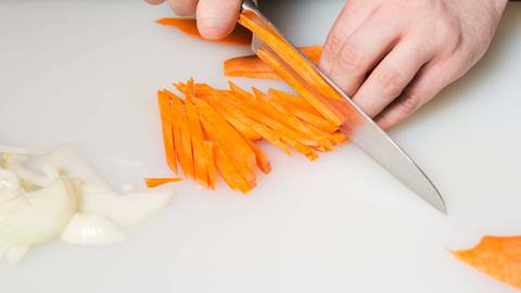 Chef cutting carrots on a cutting board.