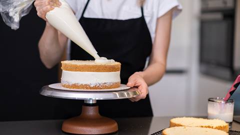 Woman decorating a cake and piping frosting.