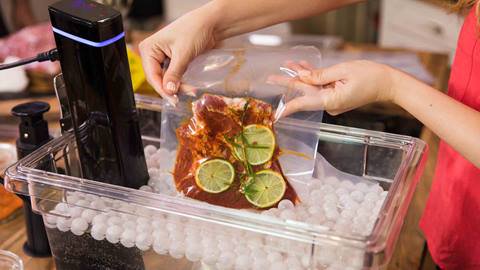 Close up of chef cooking sous vide. Raw meat with lime and rosemary in airtight vacuum sealed bag.