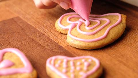 Person decorating cookies with pink piping.