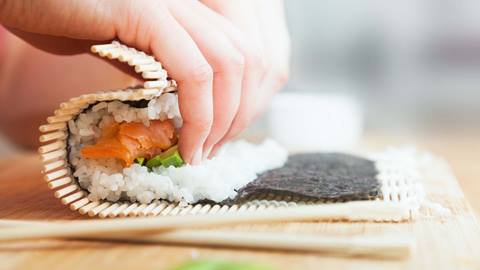 Person making a sushi roll in a cooking class.