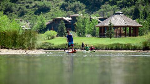 A man is paddleboarding at Deer Valley. Two young kids are paddleboarding behind him.