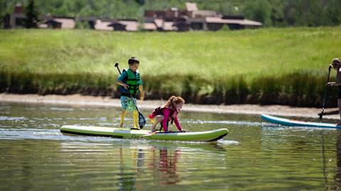 Two young kids standing on a paddleboard.