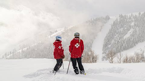 Two Deer Valley ski patrollers looking at mountain while in uniform.