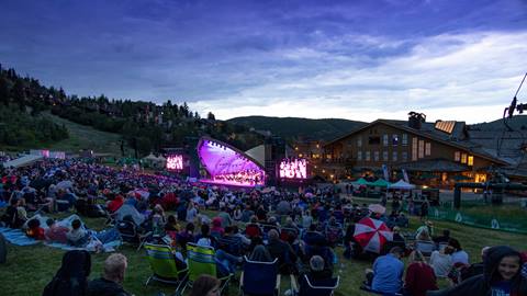 Deer Valley summer concert at dusk. A large crowd is sitting in the grass watching the concert.