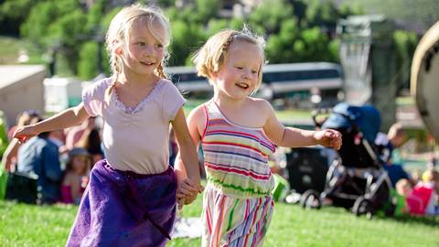 Two little girls holding hands while running at a Deer Valley summer concert.