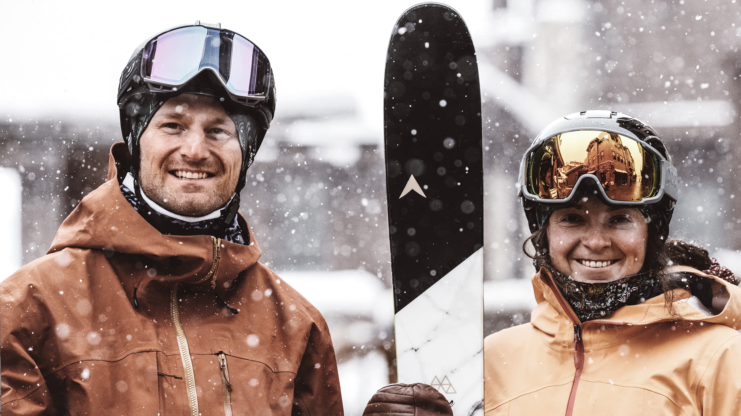 Couple smiling at camera outside with the snow falling in the background.