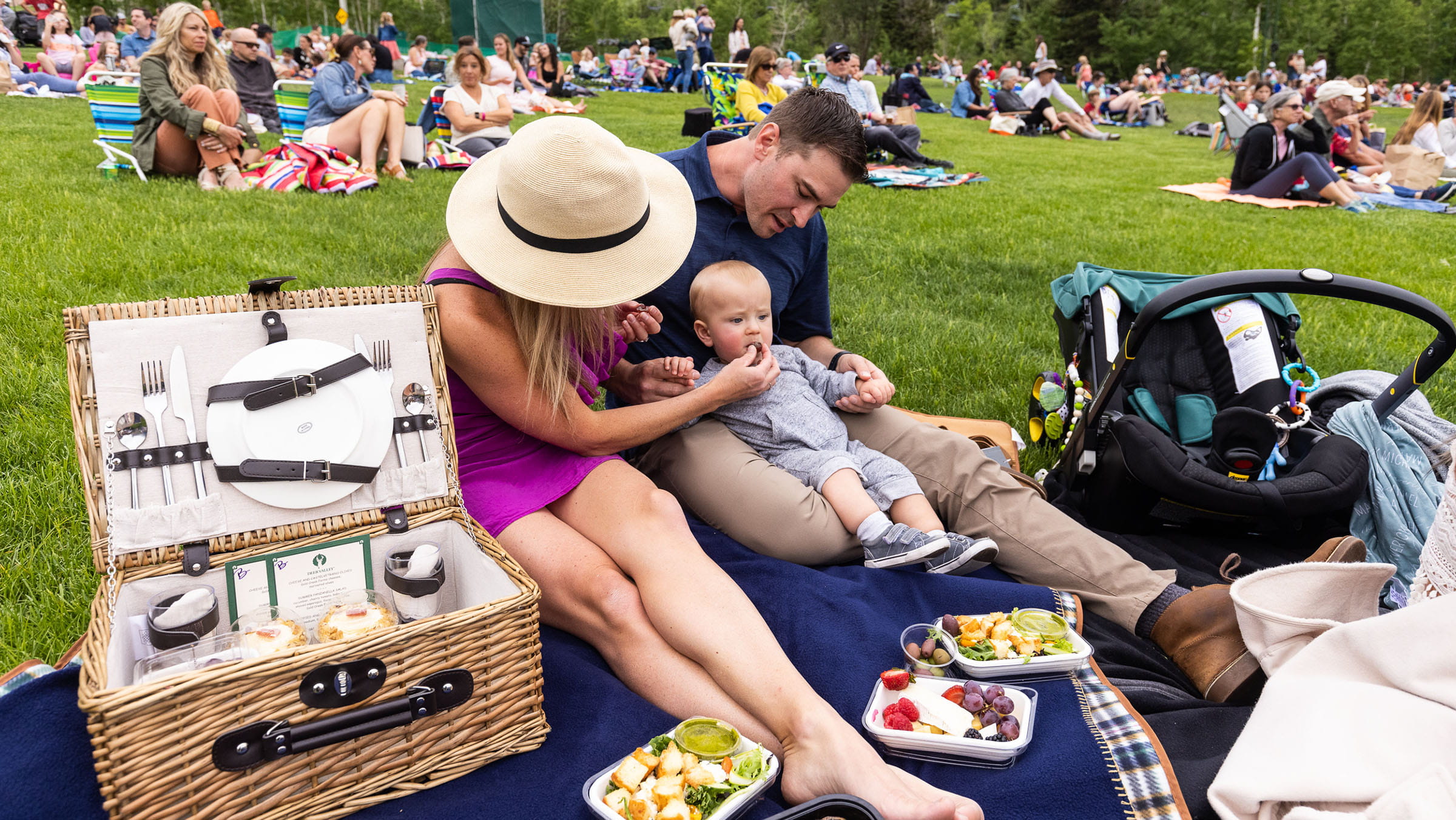 A family with a small child sitting on a blanket at an outdoor summer concert at Deer Valley.