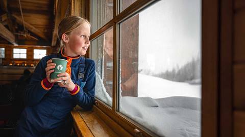 Girl drinking hot chocolate and looking out the window at Cushing's Cabin.
