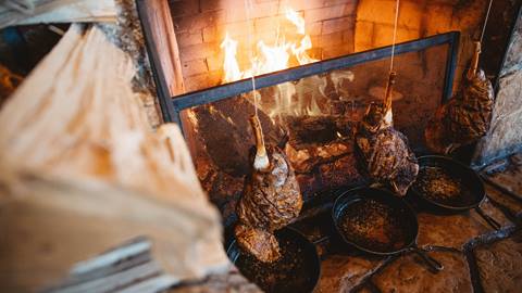 A coule legs of lamb roasting by a fireplace.