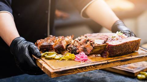 Steak and ribs served on a wooden cutting board by a chef.