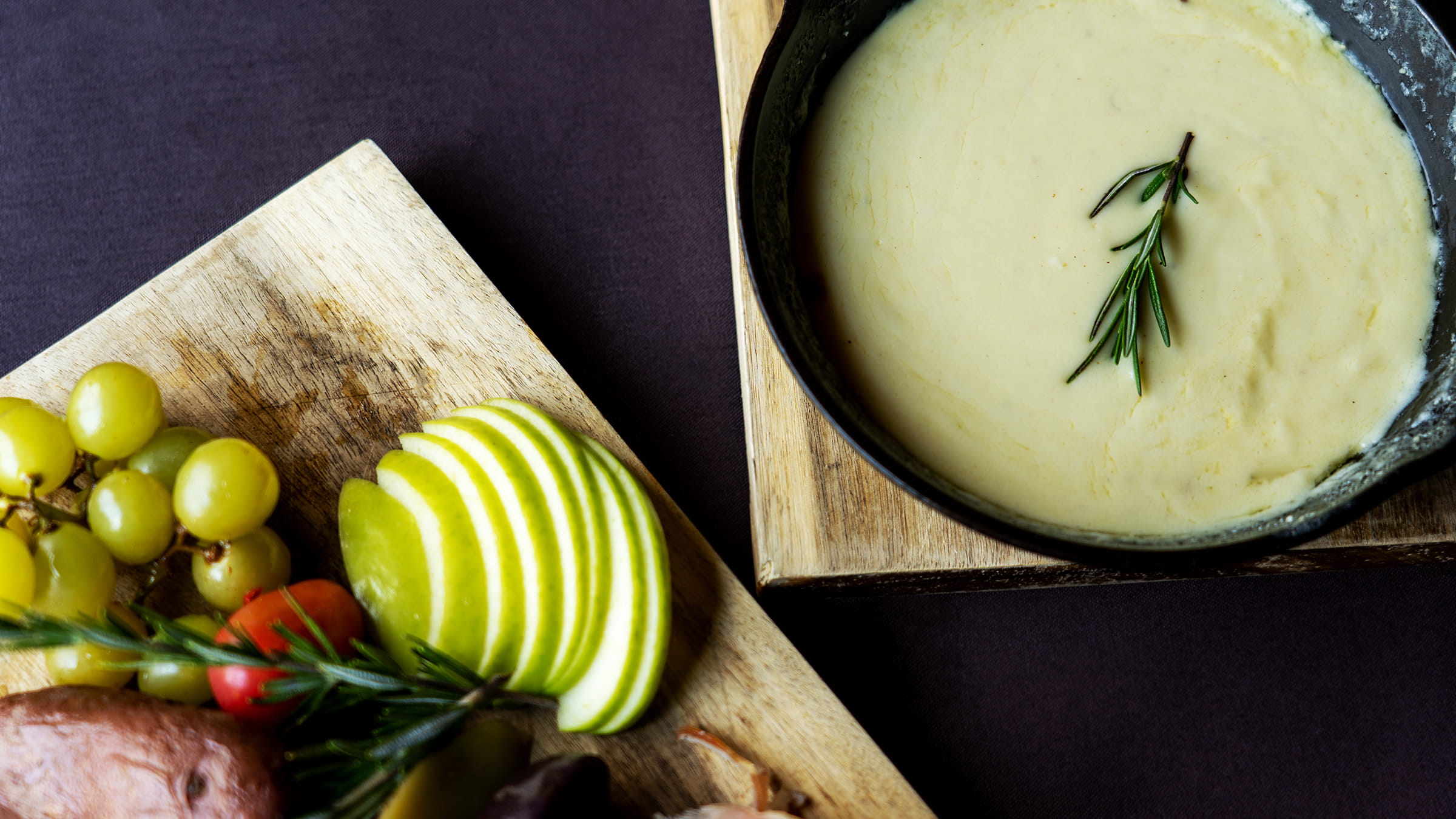 Fondue, apples, and grapes on a cutting board.