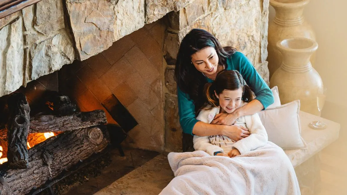 Mother and daughter sitting together next to a fireplace.