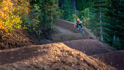 Man doing a jump on his mountain bike on a trail at Deer Valley with foliage.