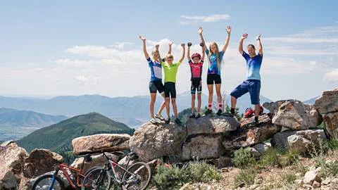 A family wearing mountain biking gear are standing on large rocks with their hands in the air.