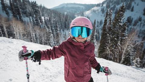 Young child wearing pink ski gear smiling outside at Deer Valley in the winter