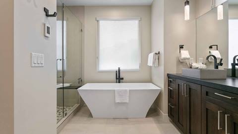 Modern freestanding soaking tub in SkyRidge 1307 primary bathroom with glass shower and dual vanity.