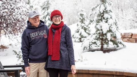 Couple wearing Deer Valley apparel are standing outside while it is snowing.