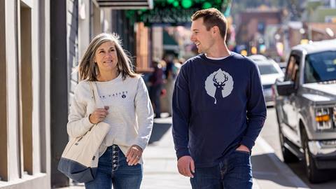 Two guests wearing Deer Valley apparel walking down Park City Historic Main Street.