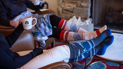 Two people wearing Deer Valley socks sitting on a couch.