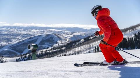 Woman in red ski outfit skiing groomed run with a view at Deer Valley.