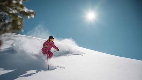 Woman in pink ski outfit skiing powder on a sunny at Deer Valley in Park City, Utah.