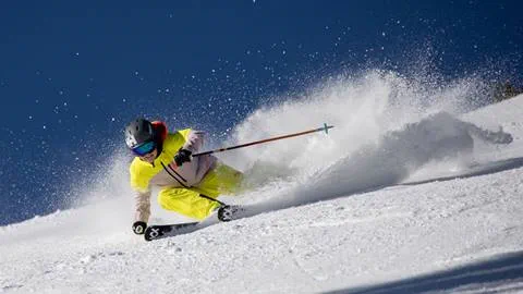 Skier in vibrant yellow ski jacket gracefully carving down the slopes at Deer Valley Resort.