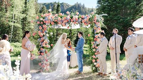 Bride and Groom standing under floral arch during wedding ceremony at Deer Valley's Orion Meadow