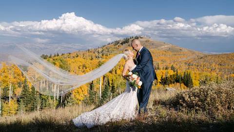 Bride and groom kissing with Deer Valley's mountain foliage behind them