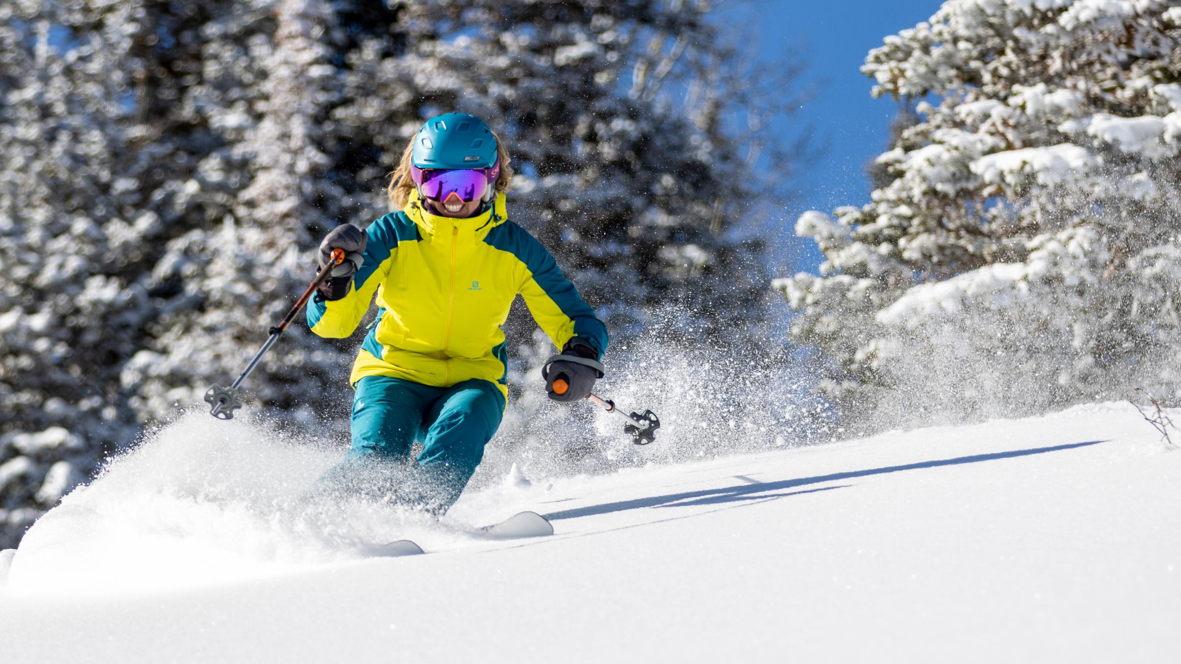 A guest in a bright jacket skiing through powder smiling