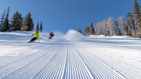 Two guests skiing a groomed run on a bluebird day at Deer Valley.