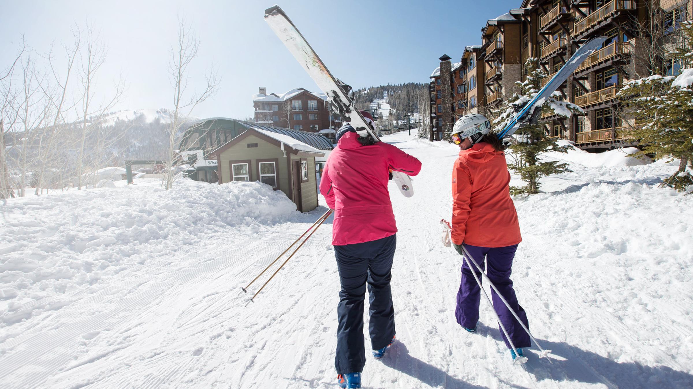 Two women walking towards the chairlift while holding their skis.