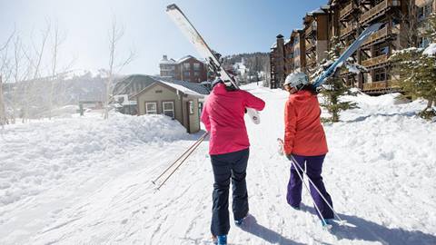 Two guests walking out of their lodging accommodations to go skiing