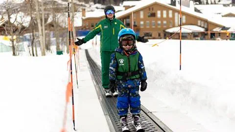 A little boy riding up the conveyor with his instructor smiling