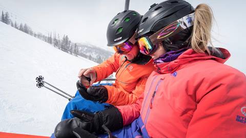 Two guests sitting on a chairlift looking at a phone