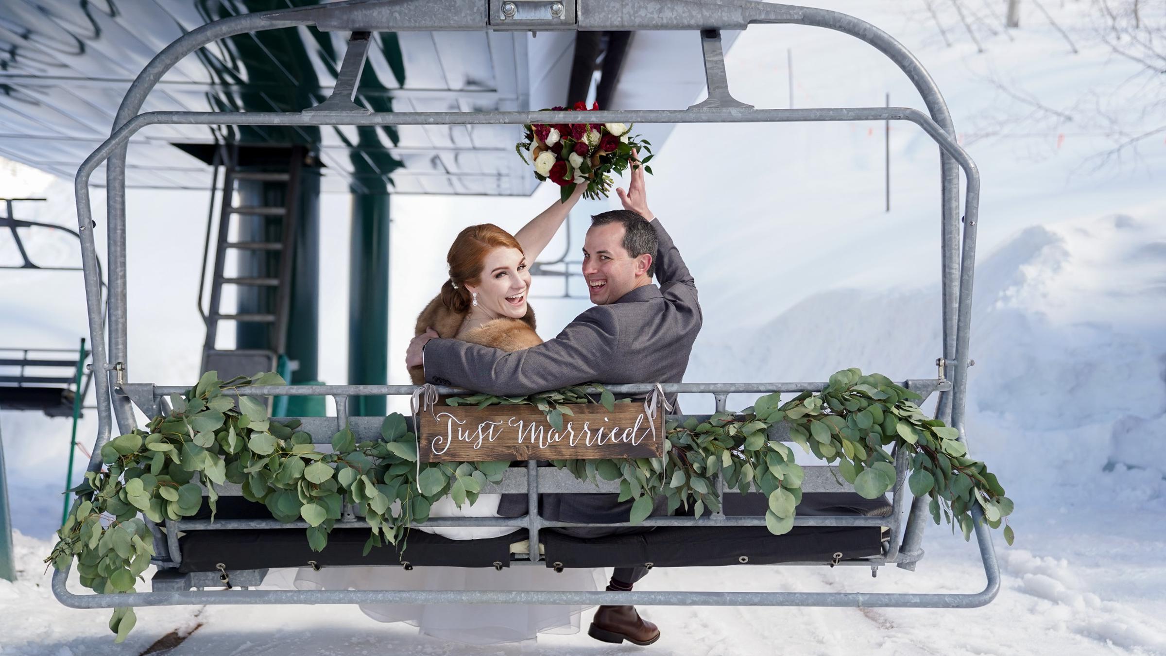 A bridge and groom sitting on a chairlift smiling