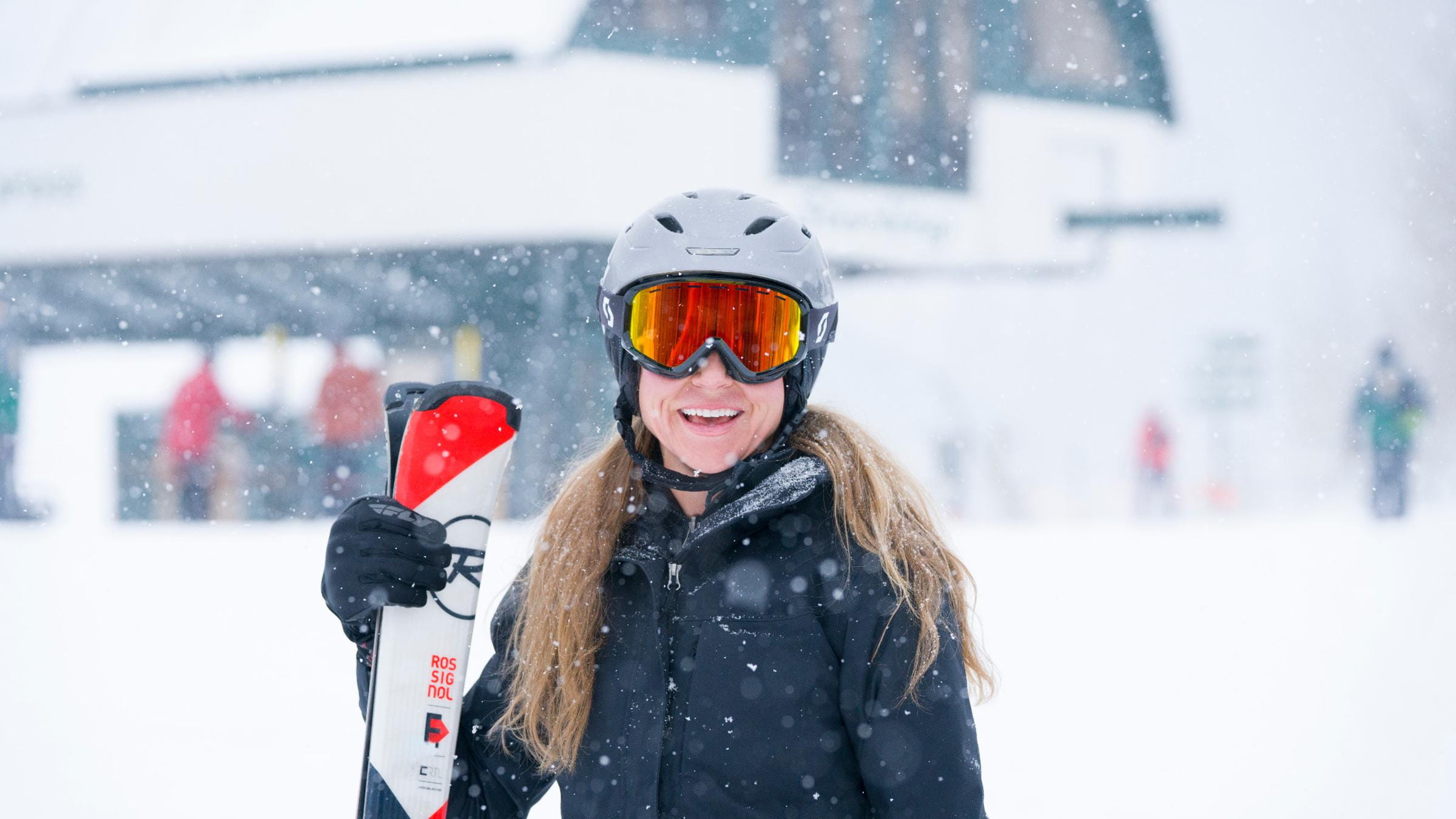 A female guest smiling and holding Rossignol Skis while it snows