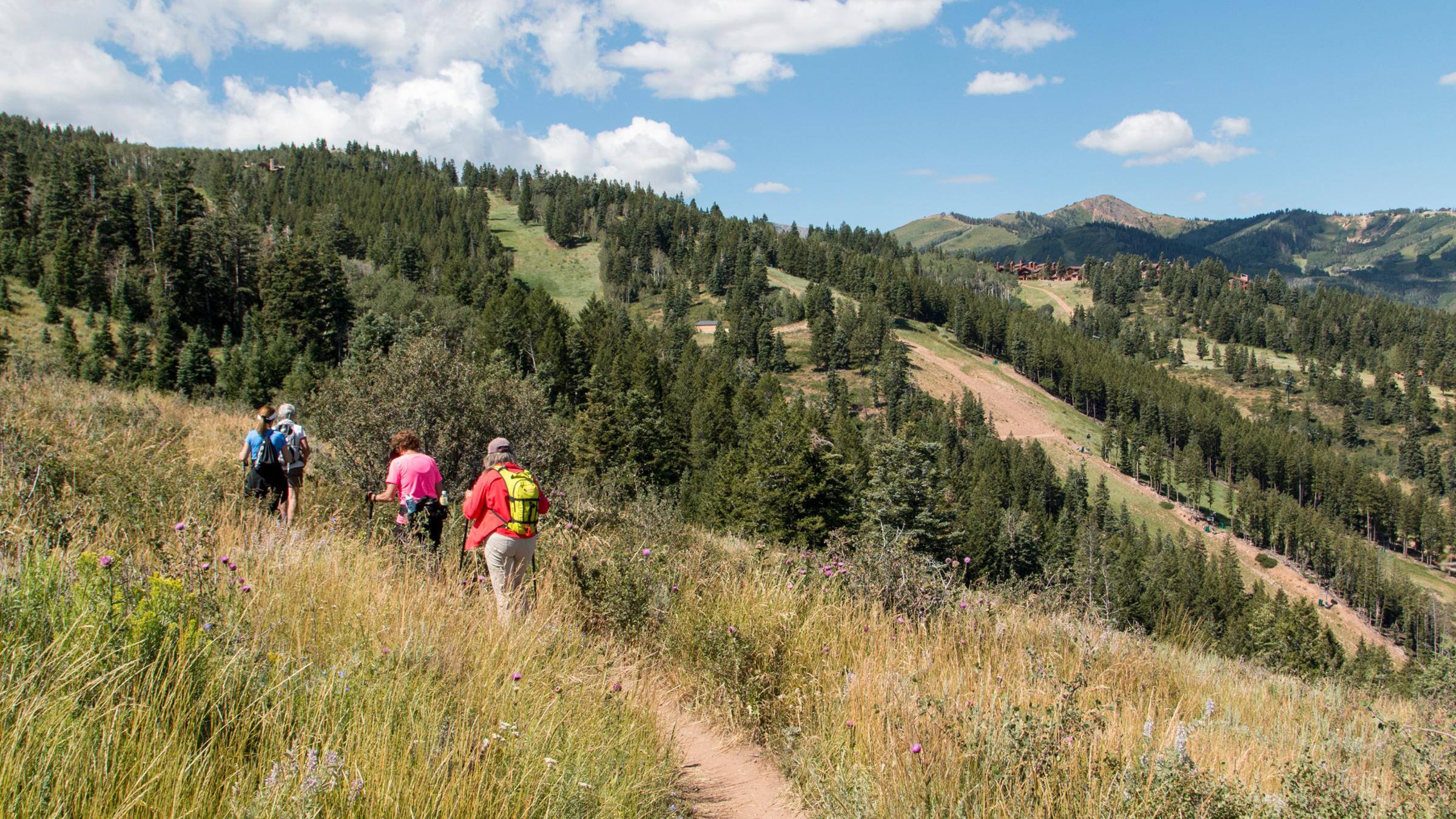 A group of guests on a guided hike at Deer Valley Resort with ski runs in the background