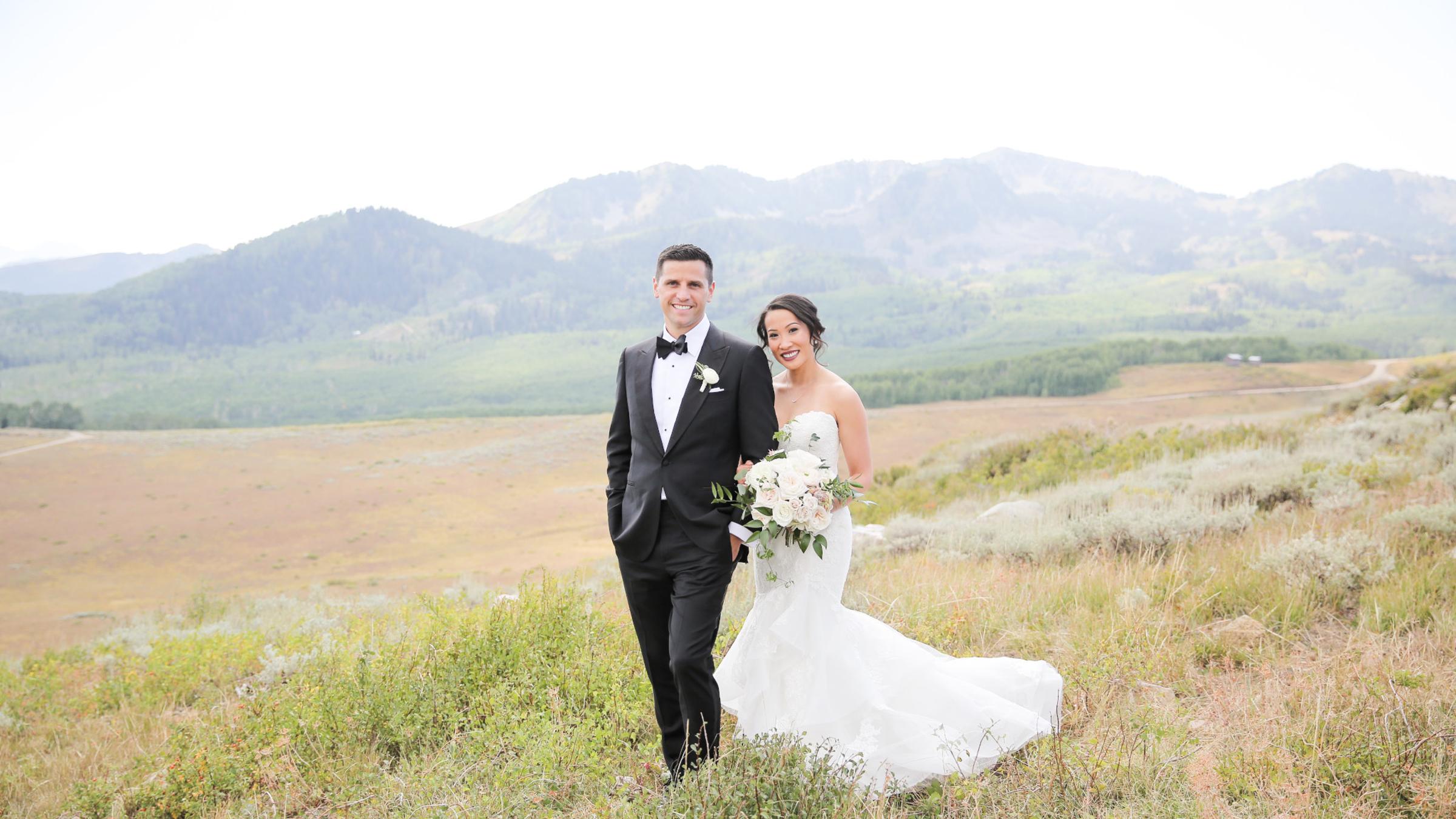 A bride and groom smiling on top of a mountain