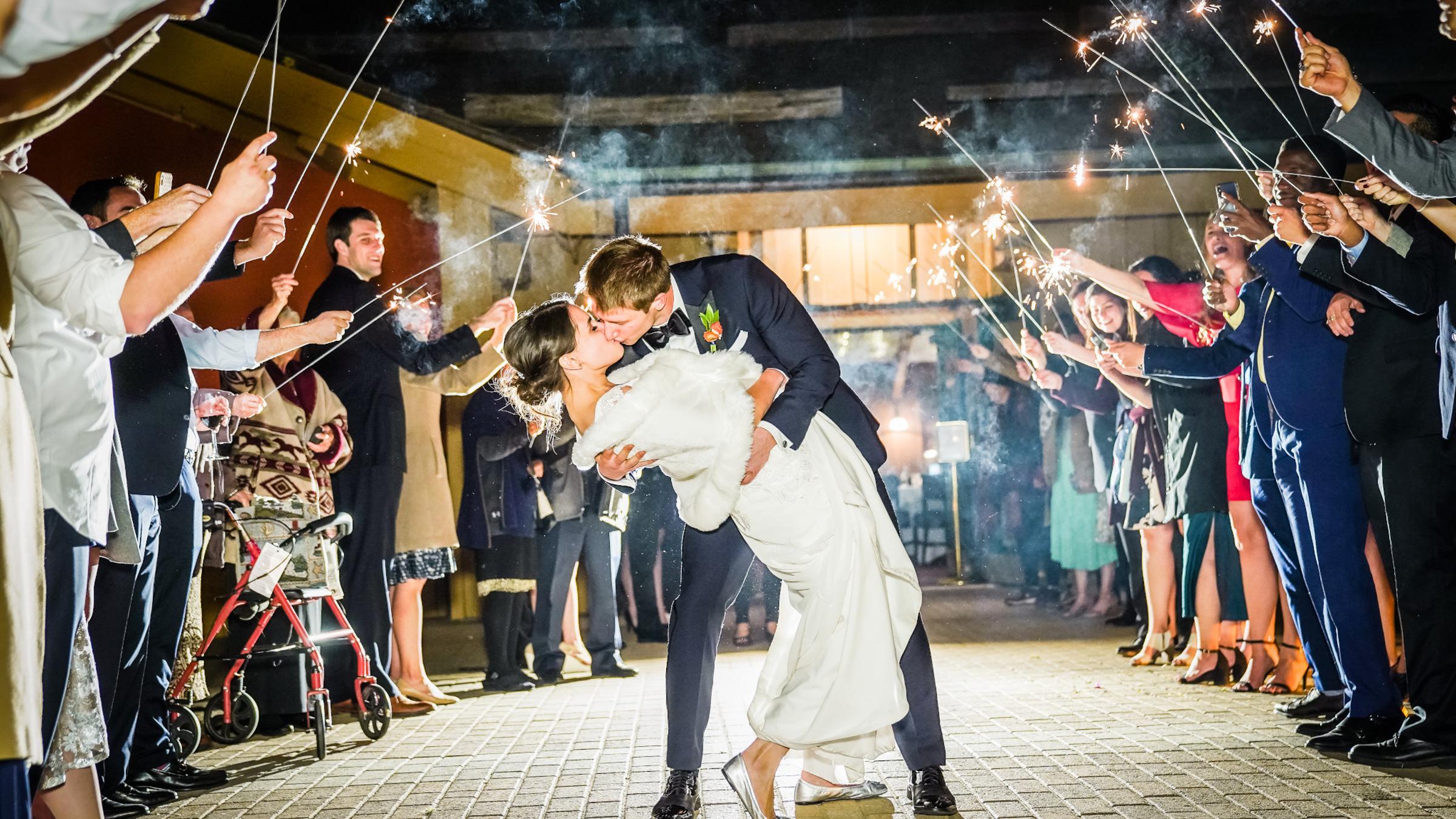 A bride and groom kissing around sparklers