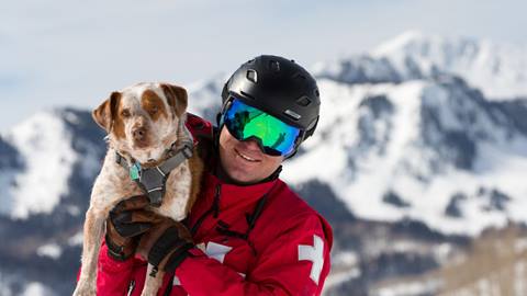 A ski patroller holding an avalanche dog over his shoulder smiling